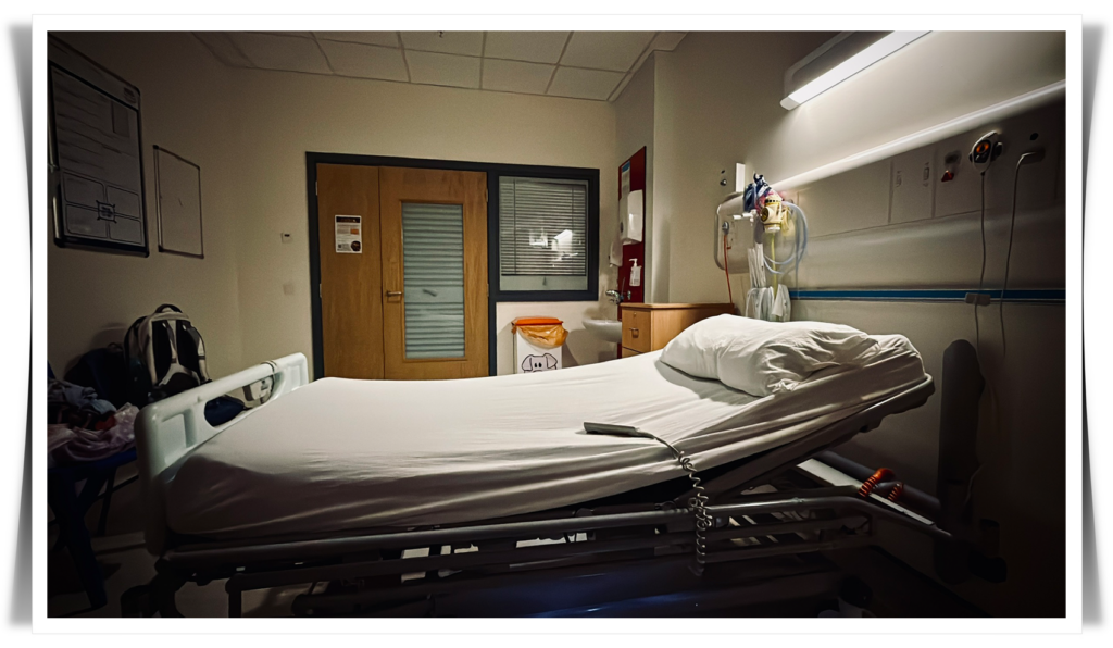 A photograph of an empty hospital bed with the reading light above it switched on.